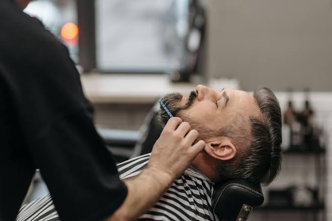 Illustrated barber shaping a client's beard with professional grooming tools